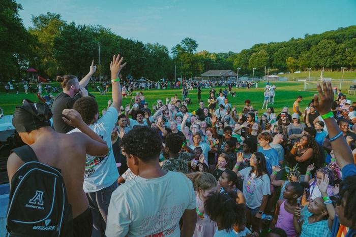 Kids and families with hands raised at an outdoor outreach