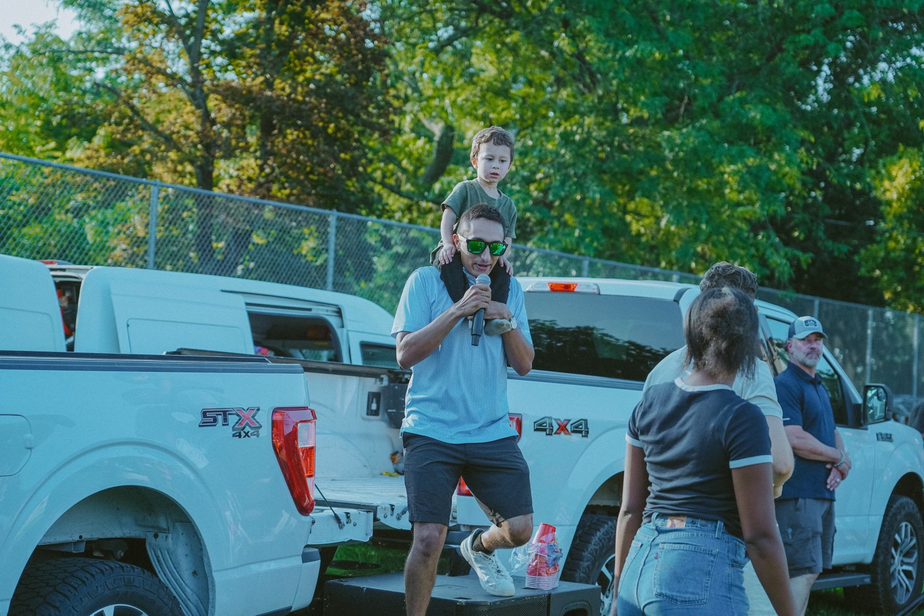 The MC on a pickup truck with speakers set up in a park
