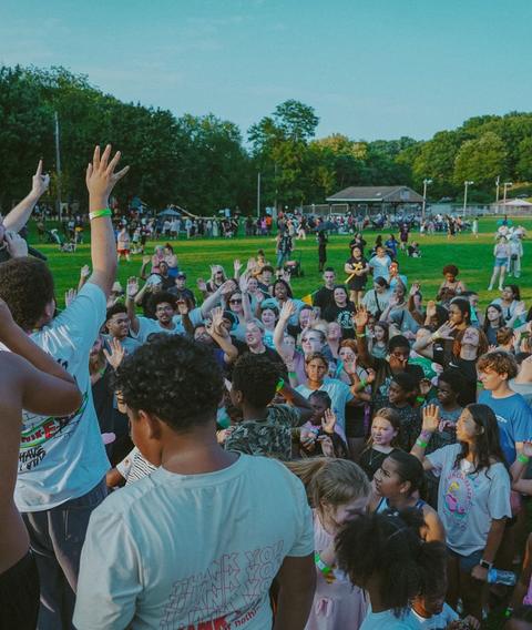 Kids and families with hands raised at an outdoor outreach
