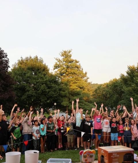 Children with hands up in front of the sound system at dusk