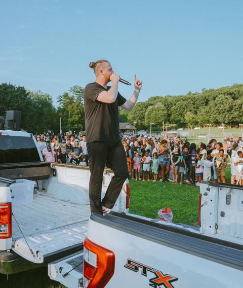 Preaching from the bed of a pickup truck to a crowd in a park